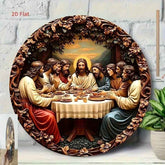 A large round decorative wall plaque depicting the Last Supper, styled as a 3D relief sculpture with an ornate carved wooden frame. The plaque is shown leaning against a white brick wall next to a potted plant.