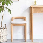 Wooden chair with white cushion next to a wooden desk and plant in a room with white walls.