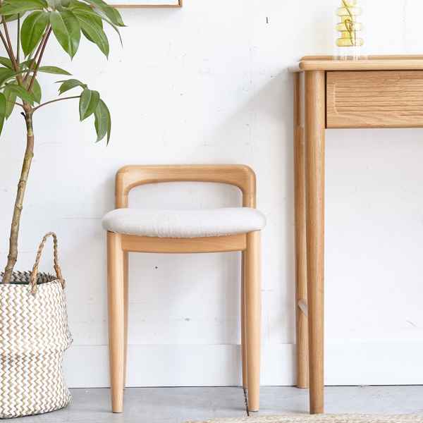 Wooden chair with white cushion next to a wooden desk and plant in a room with white walls.