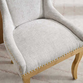 Close-up of a gray upholstered chair with wooden legs and gold nailhead trim on a light background.