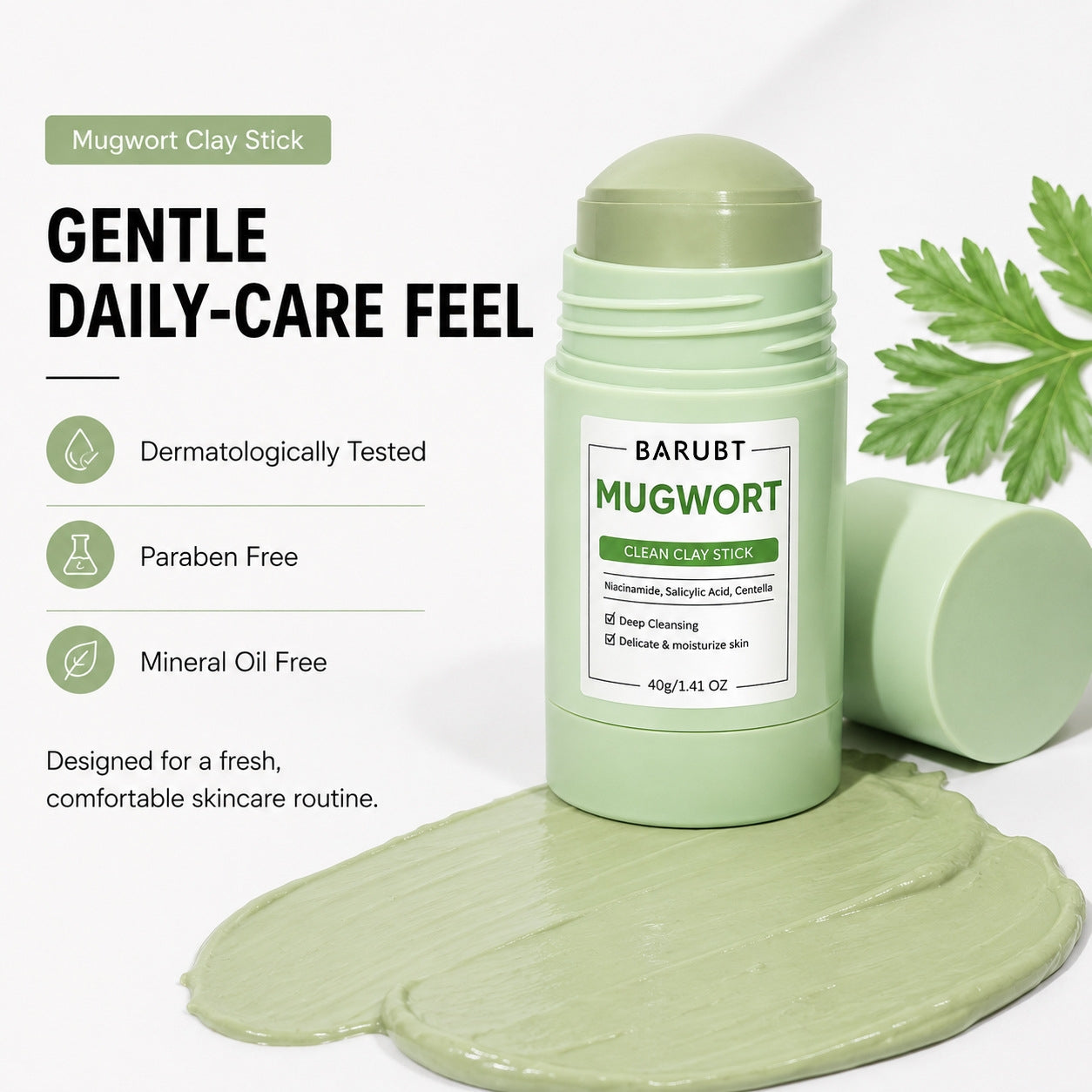 BARUBT Mugwort Clay Stick shown in a light green container with the cap off, placed on top of a smear of pale green clay product. A second cap lies beside the container, and a green mugwort leaf is visible at the upper right.