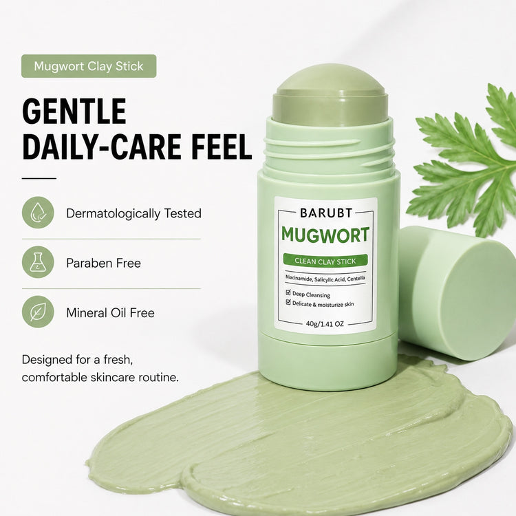 BARUBT Mugwort Clay Stick shown in a light green container with the cap off, placed on top of a smear of pale green clay product. A second cap lies beside the container, and a green mugwort leaf is visible at the upper right.