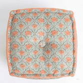 A square floor cushion or pouf with a muted sage green background and a repeating coral-orange floral pattern, finished with a solid coral-orange piped edge.