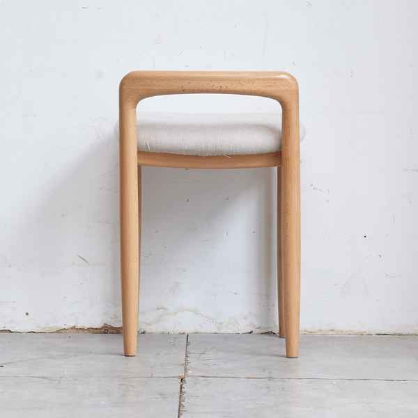 Wooden stool with a white cushion against a white wall