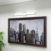 Framed cityscape artwork on a white wall with a light fixture above.