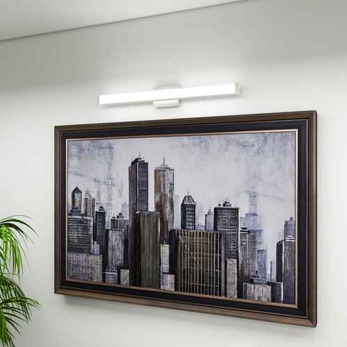 Framed cityscape artwork on a white wall with a light fixture above.