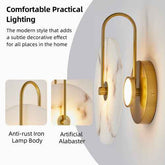 A wall-mounted sconce with a curved gold-toned metal arm and a round white-and-gray marble backplate, shown lit against a light gray wall. Text on the left reads &