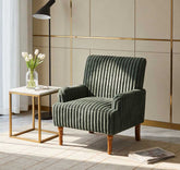 Green velvet armchair in a modern living room with a side table and lamp.
