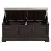 A dark brown wooden storage bench with a light beige upholstered seat cushion, shown with the lid open to reveal storage space inside.