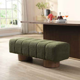An olive green boucle tufted bench with round wooden legs, positioned in a modern living room setting in front of a dark wood dining table.