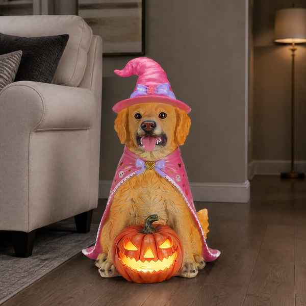 A golden retriever dog figurine dressed as a witch, wearing a pink hat and cape, sitting behind a glowing jack-o&