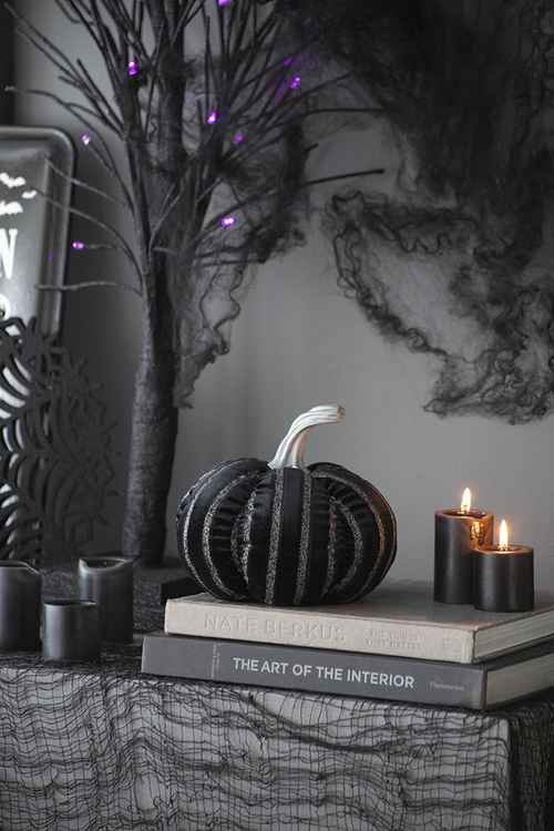 Decorative setup with black pumpkin, candles, and books on a textured surface with a dark background.