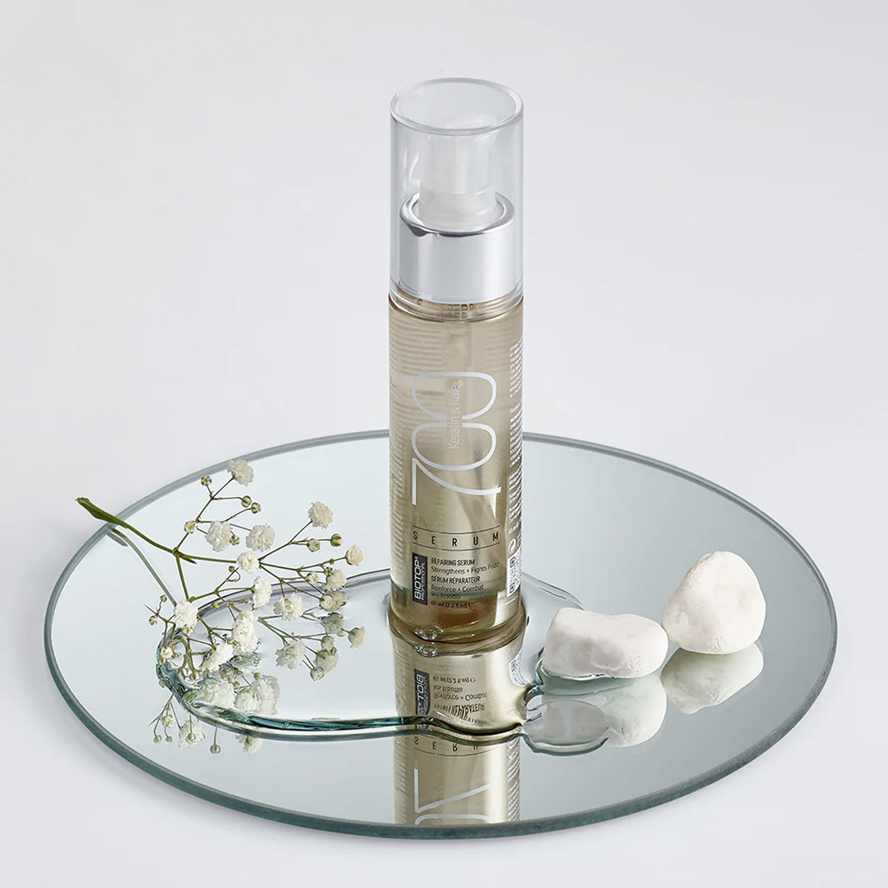 Skincare bottle with flowers and stones on a mirror surface