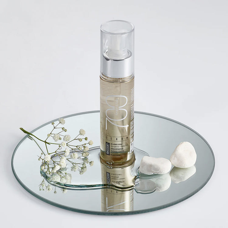 Skincare bottle with flowers and stones on a mirror surface