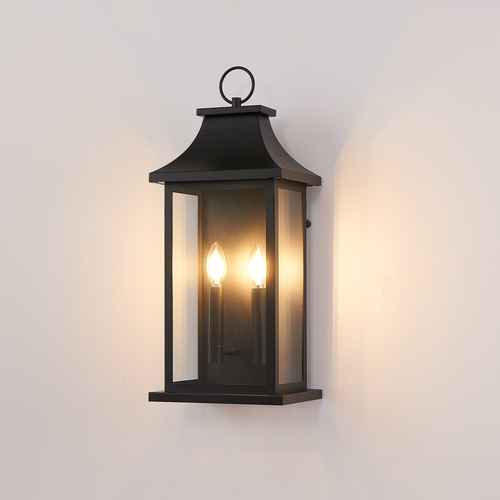 A black outdoor wall lantern light fixture with two lit candle-style bulbs, mounted on a plain off-white wall.