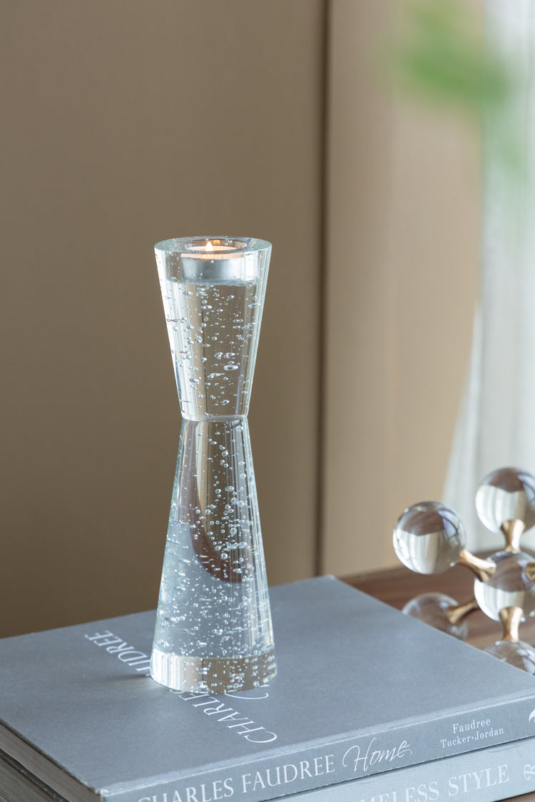 A clear glass candle holder with a flared top and dense silver glitter swirls, holding a lit tealight candle, styled on top of a gray book.