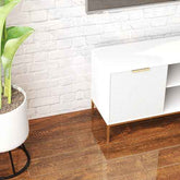 Modern white TV stand with open shelves and gold handles, positioned against a white brick wall with a potted plant nearby