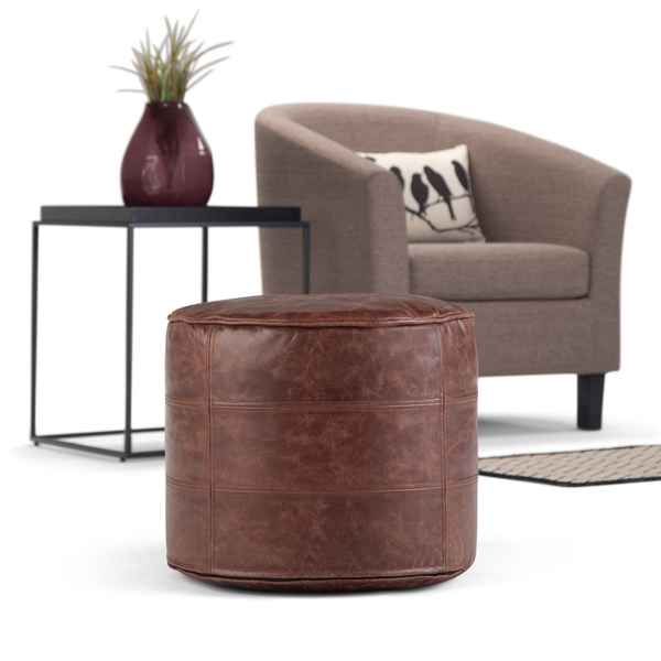 Brown leather ottoman in front of a gray armchair with a plant on a side table.