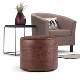 Brown leather ottoman in front of a gray armchair with a plant on a side table.