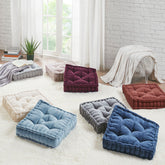 Colorful floor cushions on a light-colored rug in a room with white brick walls and large windows.