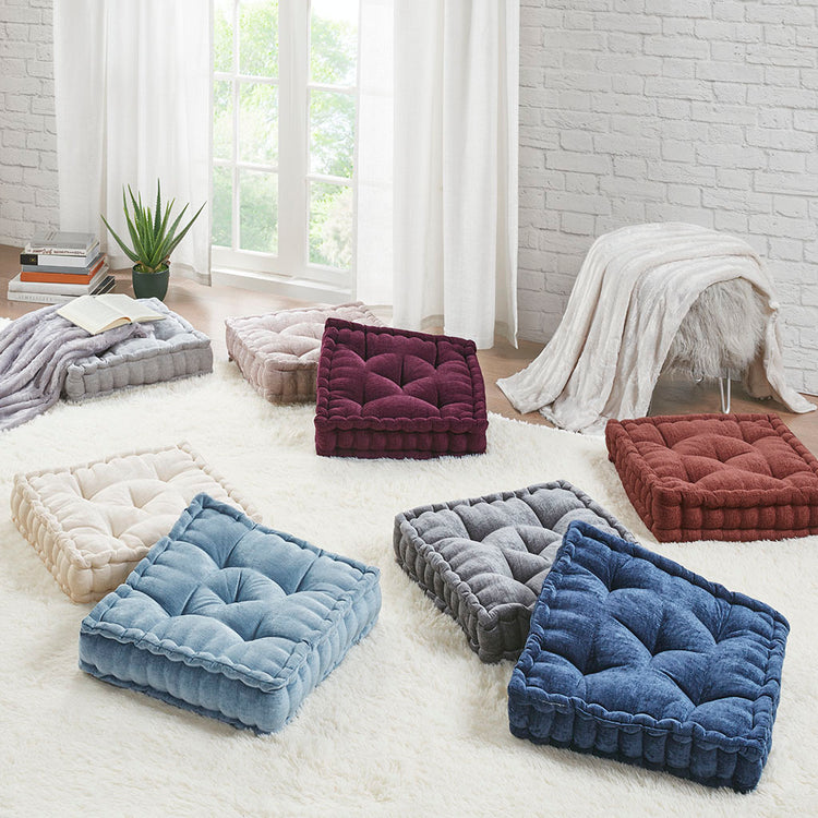 Colorful floor cushions on a light-colored rug in a room with white brick walls and large windows.