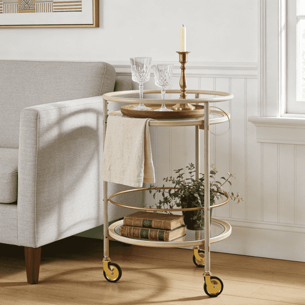 Decorative bar cart with glasses, books, and a candle in a living room setting.
