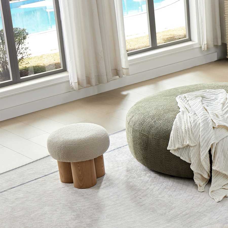 Two round ottomans, one with wooden legs and the other with a blanket draped over it, in a room with large windows.