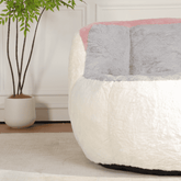 White and gray textured bean bag chair with pink accent in a room with a plant.