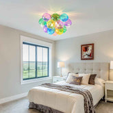Modern bedroom with colorful ceiling light fixture, bed, and window view.
