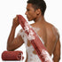 Man with soap suds on his back holding a red mesh scrubber against a white background