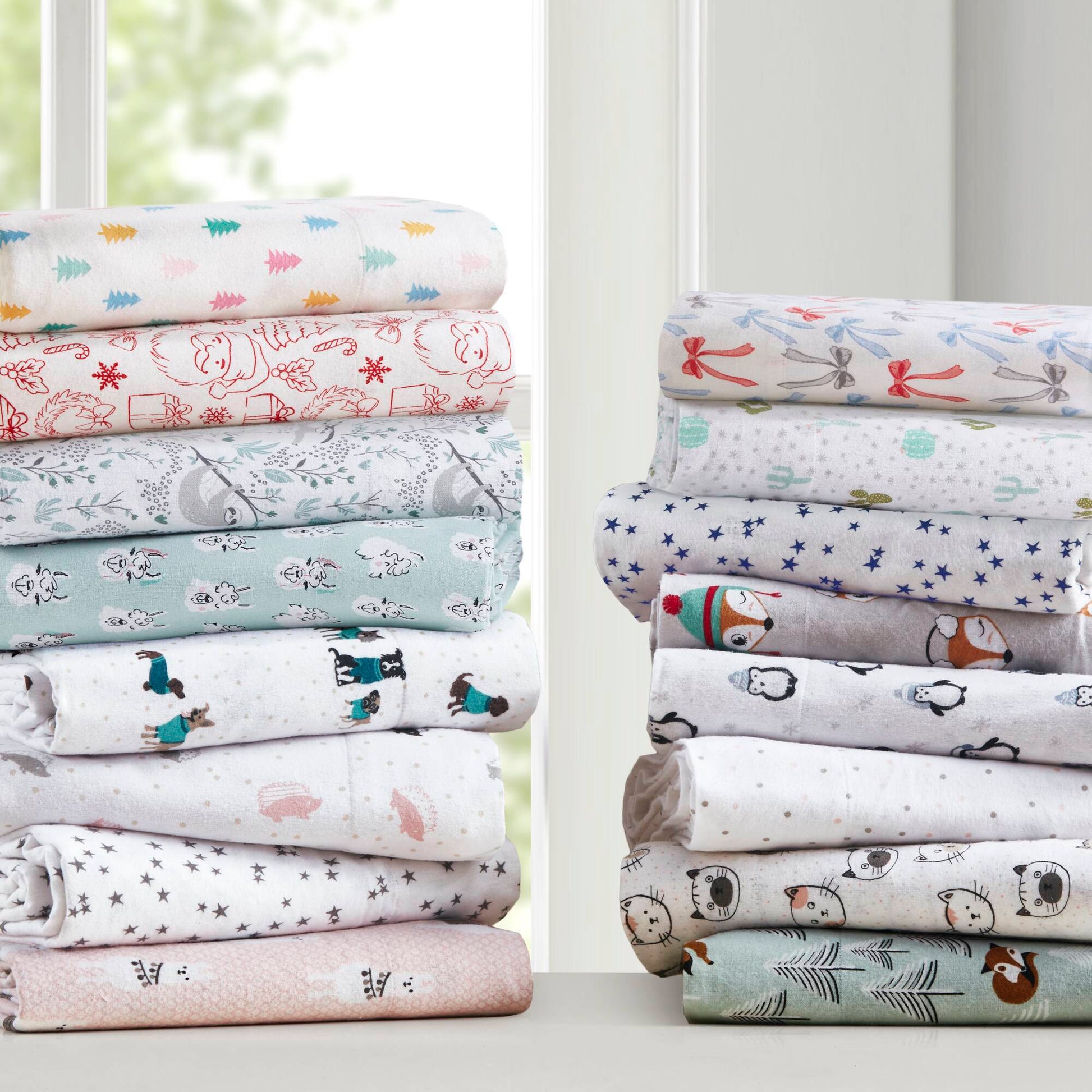 Assorted flannel sheet sets stacked by window, featuring Happy Bows Twin XL Cotton Flannel Sheet Set among other cozy, printed bedding options.
