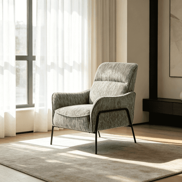 A modern upholstered accent chair in textured sage green fabric with black metal legs, positioned on a neutral rug in a brightly lit room with sheer curtains and natural sunlight.