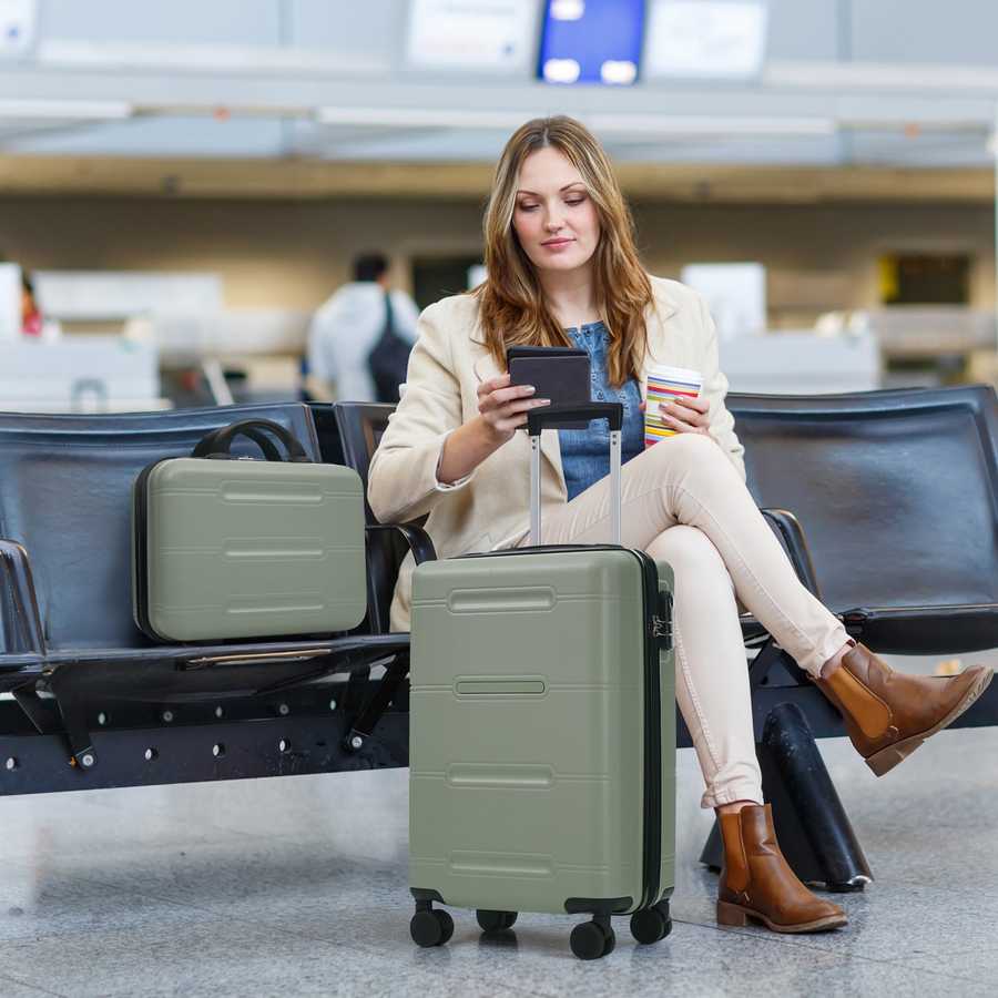 Woman sitting in an airport terminal with a suitcase and phone.