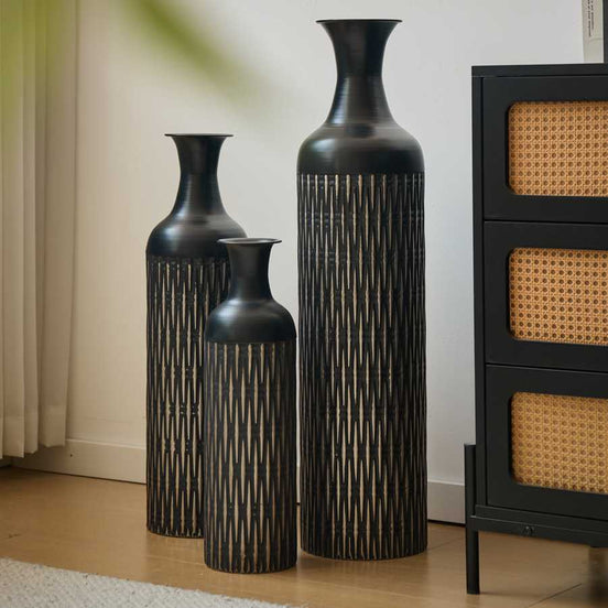 Set of 3 black floor vases with elegant textured design, displayed in a modern living room corner beside a black cabinet.