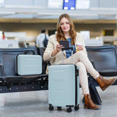Woman sitting in an airport terminal with a suitcase, using a phone.