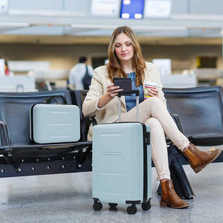 Woman sitting in an airport terminal with a suitcase, using a phone.