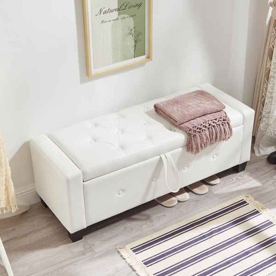 White upholstered bench with a pink blanket in a room with a striped rug and framed picture on the wall.