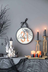 Halloween circle sign with spiderweb and October 31, displayed on a table with candles, pumpkins, and Halloween decor