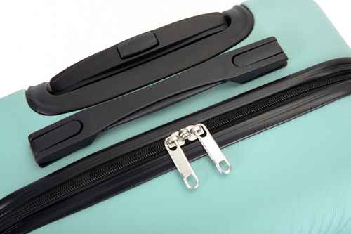 Close-up of a mint green hardshell suitcase showing a black zipper with silver metal pulls, a black telescoping handle, and a black carry strap on a white background.
