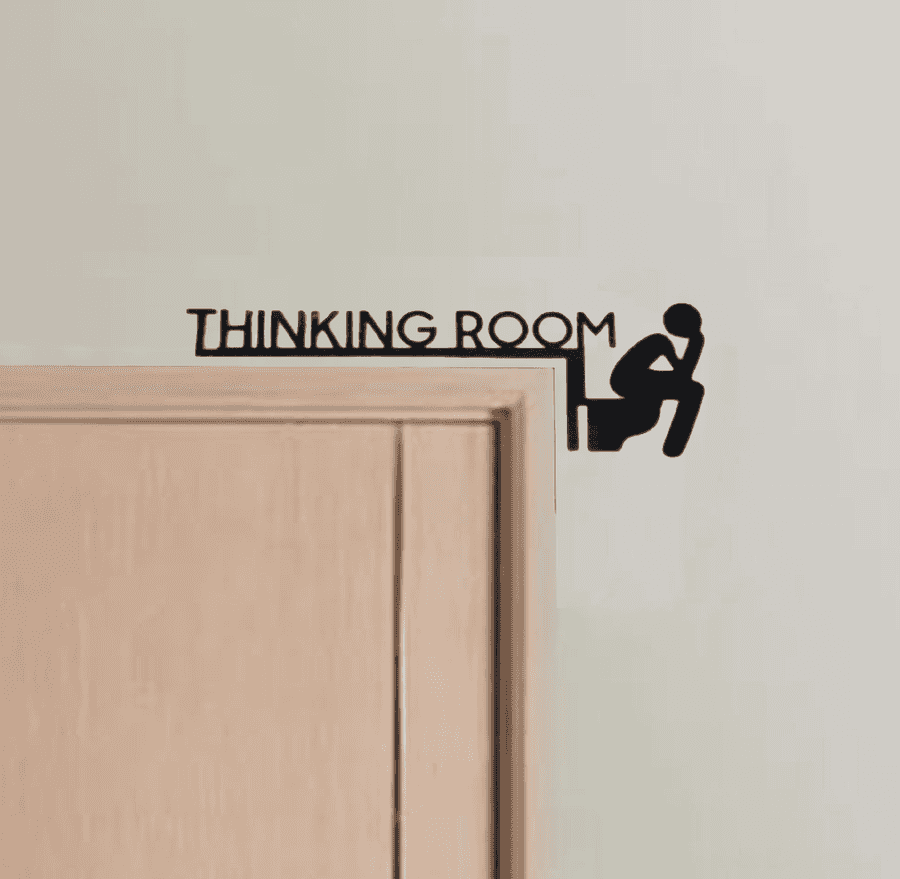 Black metal 'Thinking Room' sign in marble style mounted above a light wood door, adding humor to bathroom wall decor.