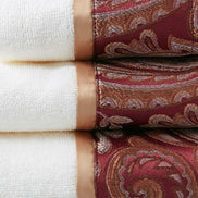 Close-up of burgundy jacquard towel set showing intricate paisley design and soft cotton texture with satin trim for luxurious bathrooms.