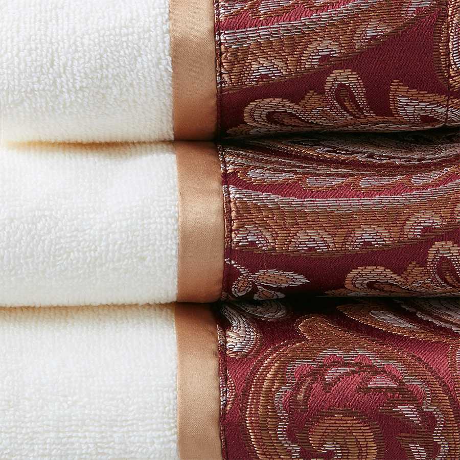Close-up of burgundy jacquard towel set showing intricate paisley design and soft cotton texture with satin trim for luxurious bathrooms.