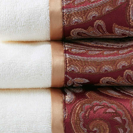 Close-up of burgundy jacquard towel set showing intricate paisley design and soft cotton texture with satin trim for luxurious bathrooms.