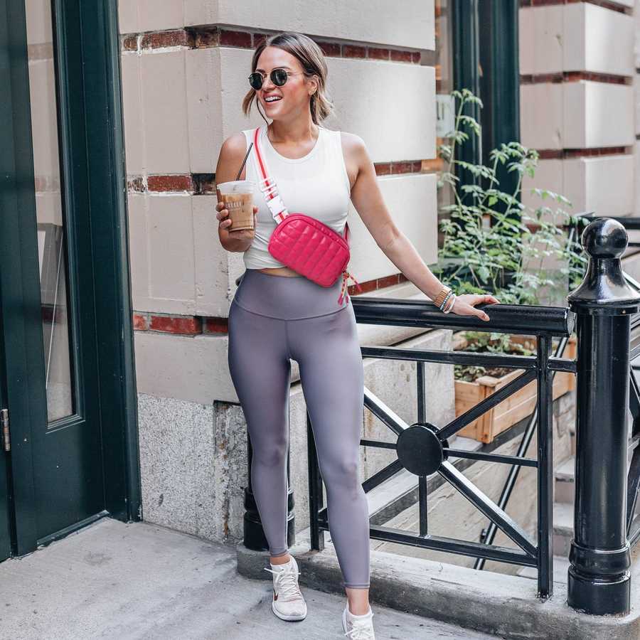 Woman in athletic wear with a pink bag and sunglasses, standing outdoors.