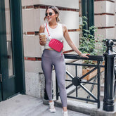 Woman in athletic wear with a pink bag and sunglasses, standing outdoors.