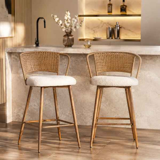 Two modern bar stools with woven cane backs and white bouclé seats, positioned in front of a stone kitchen counter.