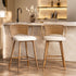 Two modern bar stools with woven cane backs and white bouclé seats, positioned in front of a stone kitchen counter.
