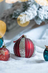 Decorative Christmas ornaments on a snowy surface with blurred tree and lights in the background