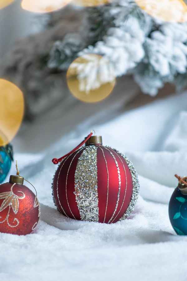 Decorative Christmas ornaments on a snowy surface with blurred tree and lights in the background
