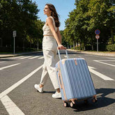 Woman walking with a blue suitcase on a road with trees in the background
